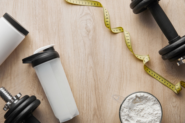 top view of dumbbells near sports bottle and measuring tape on wooden surface  - Photo, Image