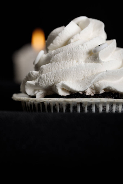 delicious Halloween cupcakes with white cream and blurred candle on background isolated on black - 写真・画像