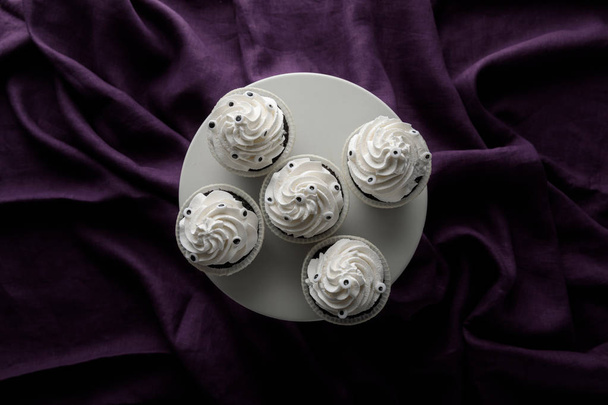 top view of delicious Halloween cupcakes with white cream on stand on purple cloth - Foto, imagen