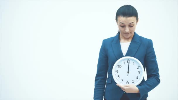 Young good teacher standing on a white background. Holds the white clock and plug. Shows the time to eat. - Materiaali, video