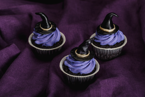 tasty Halloween cupcakes with blue cream and decorative witch hats on purple cloth - 写真・画像