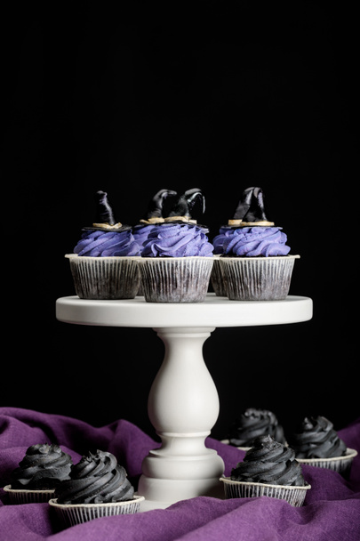 tasty Halloween cupcakes on white stand on purple cloth isolated on black - Foto, afbeelding