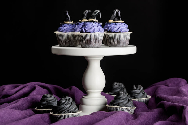 tasty Halloween cupcakes on white stand on purple cloth isolated on black - Foto, Imagen