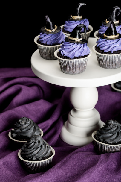 tasty Halloween cupcakes on white stand on purple cloth isolated on black - Fotó, kép