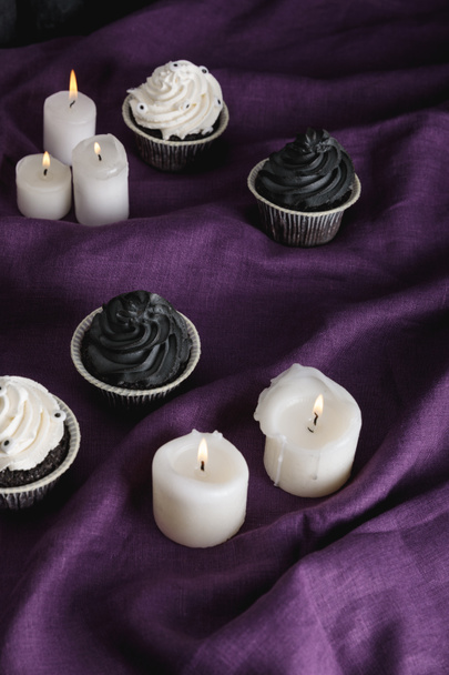 tasty Halloween cupcakes near burning candles on purple cloth - Photo, Image