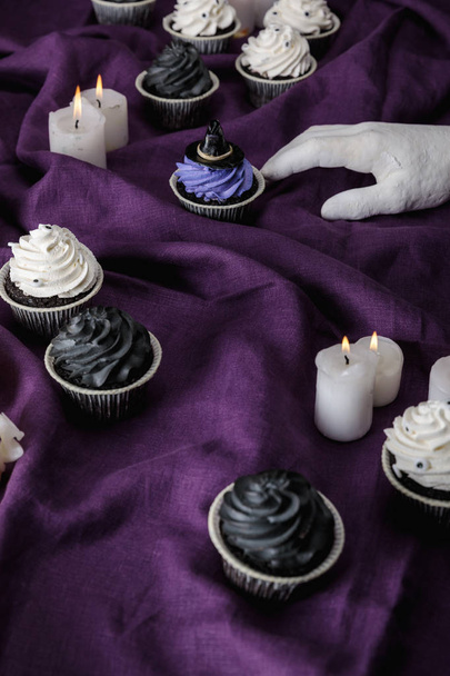 mano decorativa cerca de sabrosos cupcakes de Halloween y velas encendidas en tela púrpura
 - Foto, Imagen