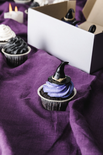 tasty Halloween cupcake with blue cream and decorative witch hat on purple cloth - Zdjęcie, obraz