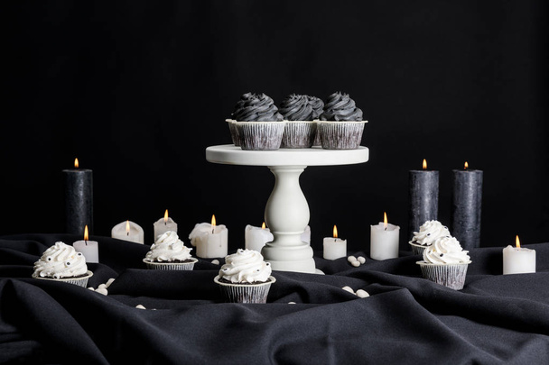 Halloween cupcakes with black cream on white stand near burning candles isolated on black - Photo, Image
