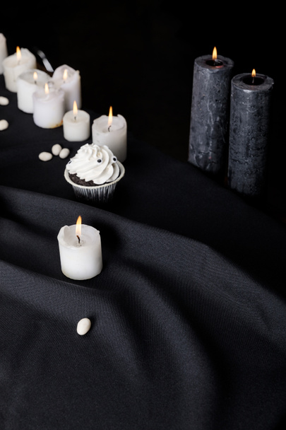 tasty Halloween cupcake with white cream near burning candles on black background - Photo, Image