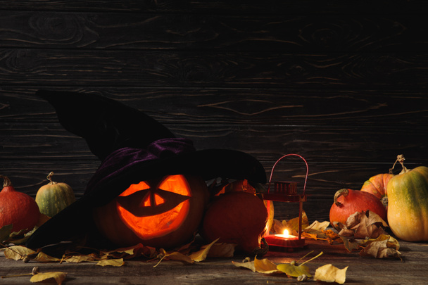 carved spooky Halloween pumpkin, autumnal leaves and burning candle on wooden rustic table on black background - Photo, Image