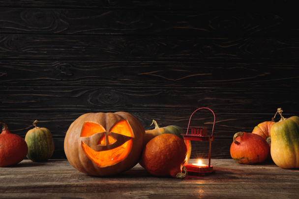 carved spooky Halloween pumpkin and burning candle on wooden rustic table on black background - 写真・画像