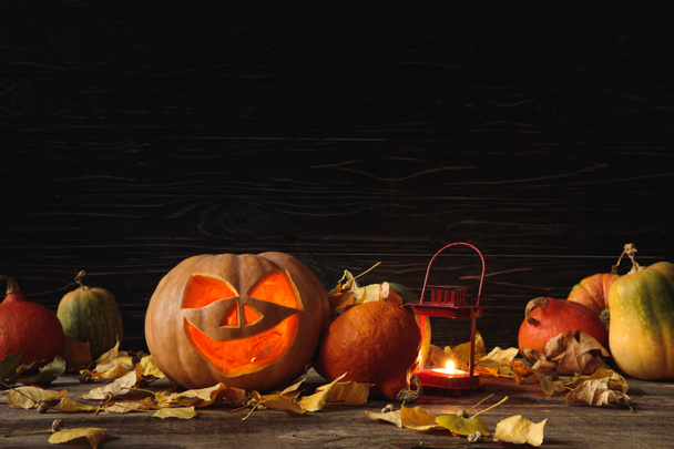 carved spooky Halloween pumpkin, autumnal leaves and burning candle on wooden rustic table on black background - Foto, Imagen