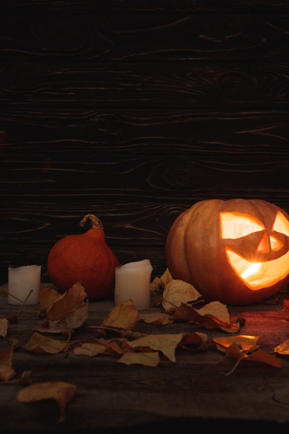 carved spooky Halloween pumpkin, autumnal leaves and candles on wooden rustic table - Fotografie, Obrázek