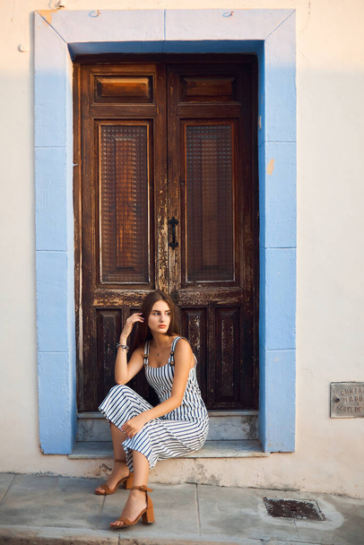 Young stylish woman sitting against old wooden doorway on the street. - Fotografie, Obrázek