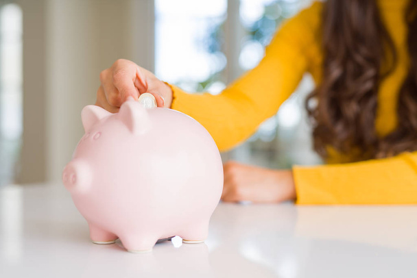 Close-up de mulher colocando uma moeda dentro do banco porquinho como investimento
 - Foto, Imagem