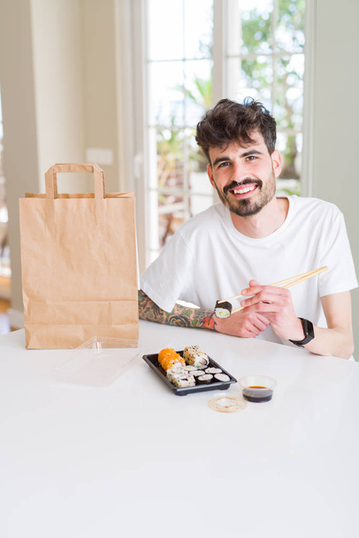 Junger Mann isst Sushi und Nudeln mit Essstäbchen  - Foto, Bild