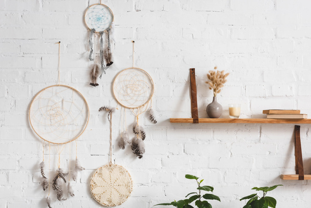 dream catchers with feathers and shelves with books on white brick wall - Photo, Image