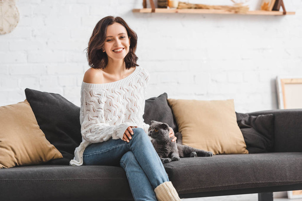 beautiful smiling girl sitting on sofa with scottish fold cat   - 写真・画像