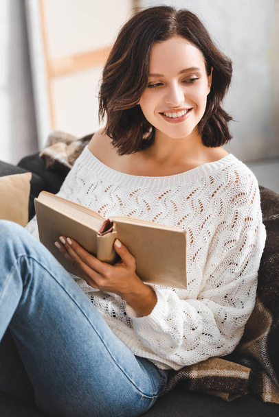 beautiful cheerful girl reading book on sofa at home - Foto, afbeelding
