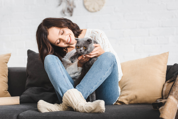 happy woman sitting on sofa with grey scottish fold cat   - 写真・画像