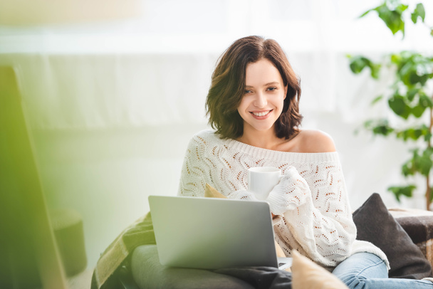 attractive smiling girl with cup coffee of using laptop at cozy home - Valokuva, kuva