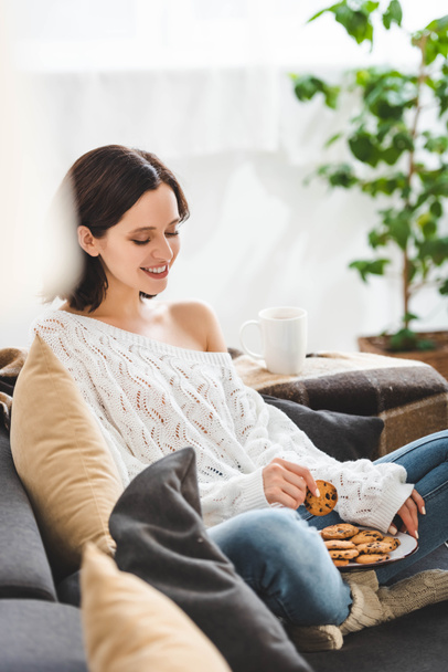 красива щаслива жінка сидить на дивані з печивом
 - Фото, зображення