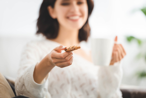 selective focus of happy girl with cup of coffee holding cookie - Фото, зображення