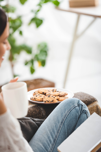 selective focus of woman reading book on sofa with tea and cookies - Foto, Imagem