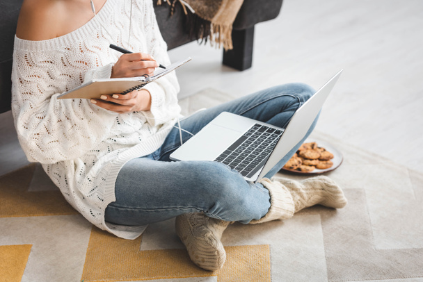 bijgesneden weergave van meisje met koptelefoon studeren online met laptop en schrijven in notebook thuis - Foto, afbeelding