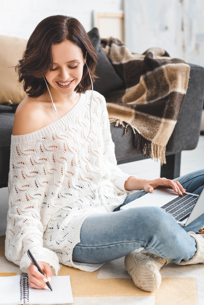 cheerful girl with earphones studying online with laptop and notebook at home - Foto, Bild