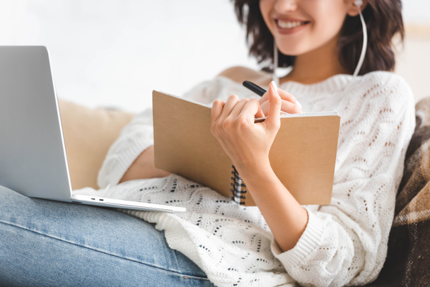 обрезанный вид улыбающейся девушки, которая пишет в блокноте и учится онлайн с ноутбуком
 - Фото, изображение