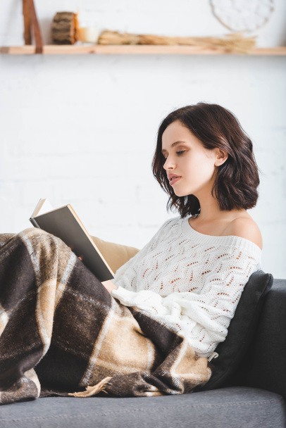 beautiful girl in blanket reading book on sofa at home - Photo, image