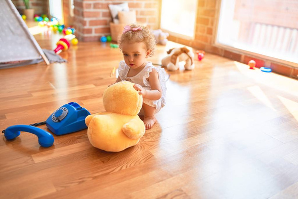 Beautiful caucasian infant playing with toys at colorful playroom. Happy and playful cuddling stuffed animal at kindergarten. - Photo, Image