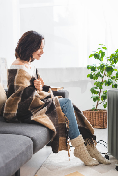 beautiful happy girl with blanket warming up with heater in cold room - Photo, image