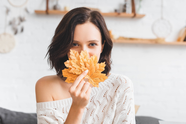 beautiful woman holding yellow autumn leaves in front of face  - Foto, imagen