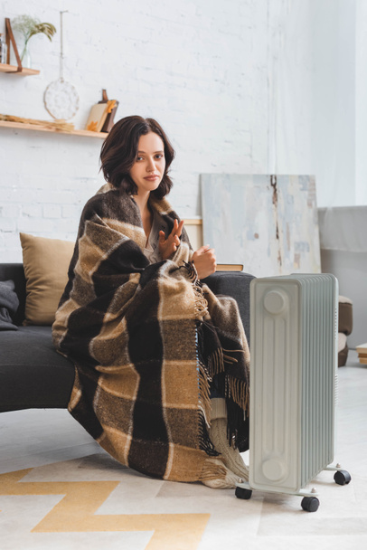 beautiful cold woman with blanket warming up near heater - Fotó, kép