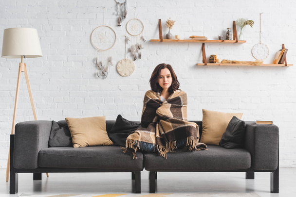 attractive cold girl warming up with blanket on sofa in living room with dream catchers - Foto, Imagem