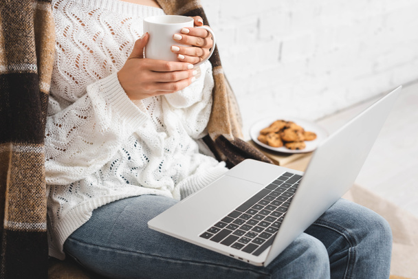cropped view of girl with cookies and coffee using laptop - Valokuva, kuva