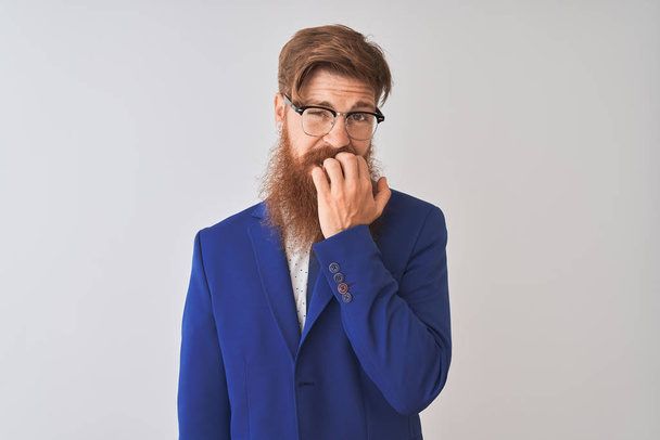 Young redhead irish businessman wearing suit and glasses over isolated white background looking stressed and nervous with hands on mouth biting nails. Anxiety problem. - Photo, Image
