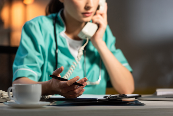 cropped view of nurse in uniform talking on telephone during night shift - 写真・画像