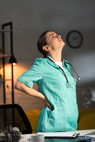 enfermeira atraente em uniforme tendo dor nas costas durante o turno da noite
 - Foto, Imagem