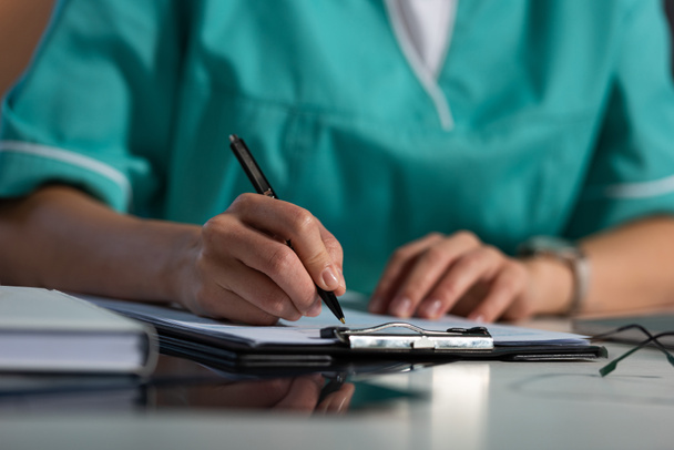 cropped view of nurse in uniform writing in clipboard during night shift - 写真・画像