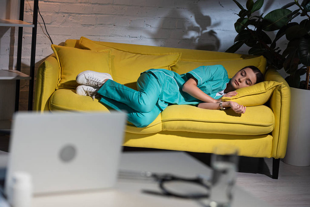 enfoque selectivo de enfermera atractiva en uniforme durmiendo en sofá amarillo durante el turno de noche
 - Foto, imagen