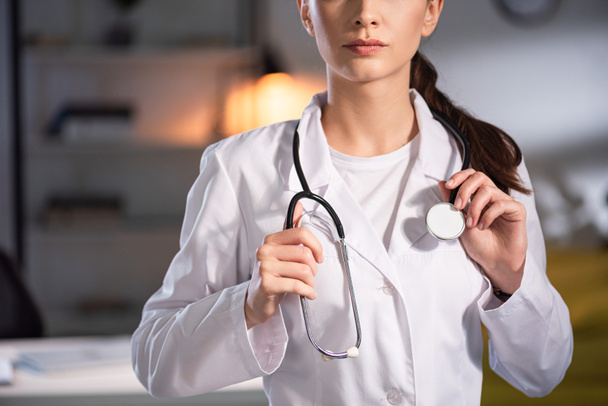 cropped view of doctor in white coat holding stethoscope during night shift - Foto, Imagen
