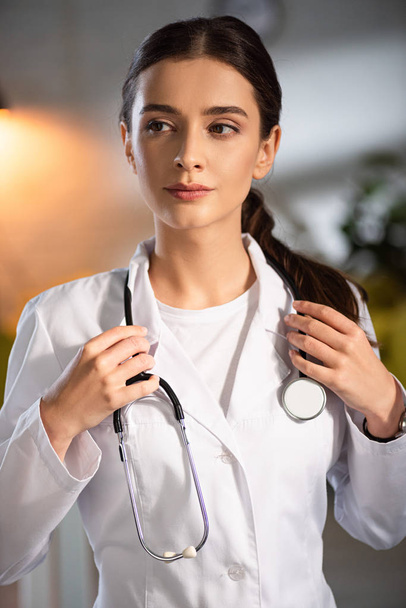 attractive doctor in white coat holding stethoscope during night shift - Foto, immagini