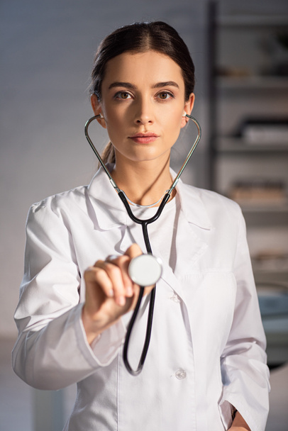 selective focus of doctor in white coat holding stethoscope during night shift - Fotó, kép