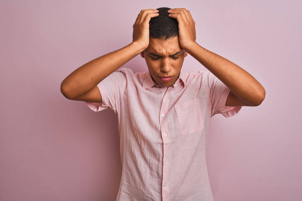 Jonge knappe arabische man draagt casual shirt staan over geïsoleerde roze achtergrond lijdt aan hoofdpijn wanhopig en gestrest omdat pijn en migraine. Handen op het hoofd. - Foto, afbeelding