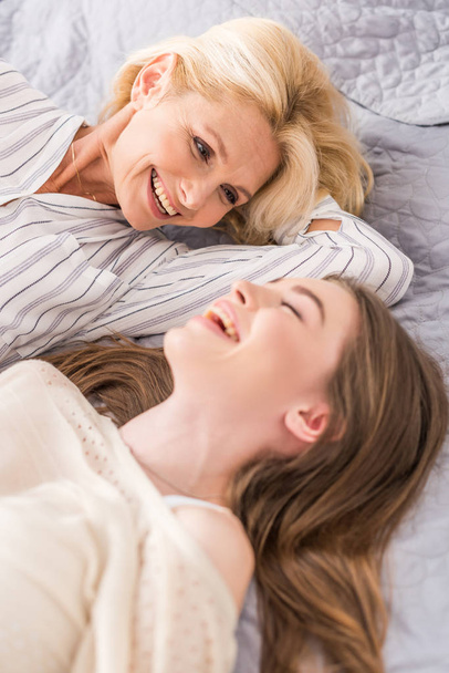 selektywny ostrość z szczęśliwy Dojrzałe kobieta patrząc na laghing córka podczas leżąc na łóżku razem  - Zdjęcie, obraz