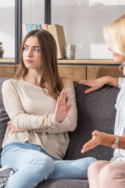 offended girl showing stop gesture and looking away while sitting near talking mother - Photo, Image