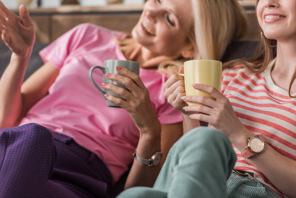 selective focus of cheerful woman pointing with hand while sitting near daughter with tea cups - Photo, Image